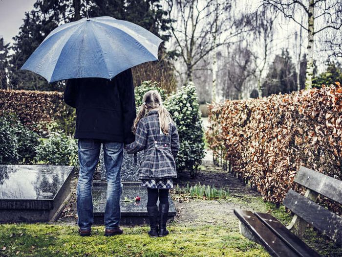 Grieving widower and daughter standing at a grave