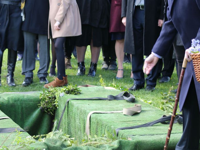 Mourners scatter soil and flowers in a grave