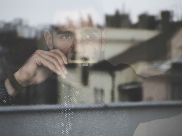 A bereaved man lost in thought gazes out of a window