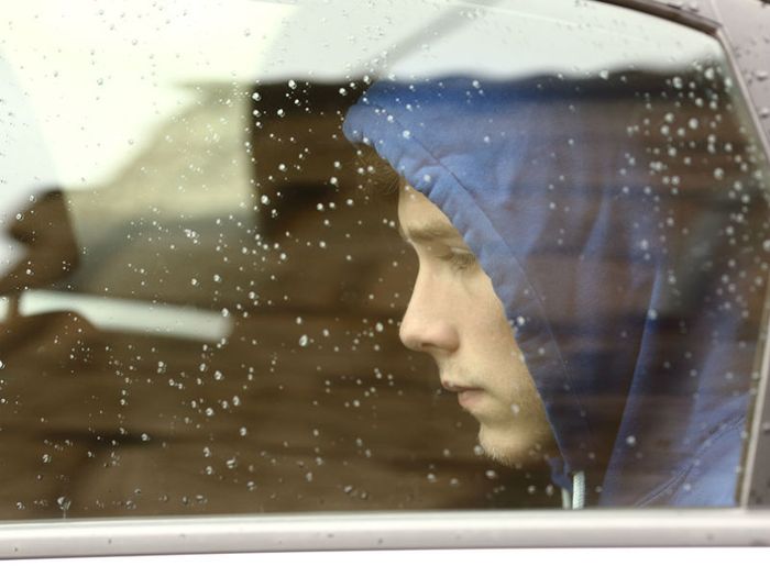 Bereaved young man sitting in car, looking out of the window