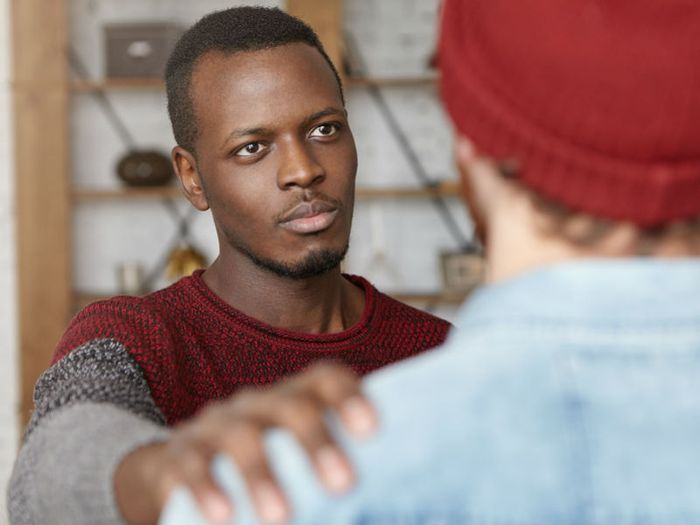 A man places his hand on a friend's shoulder in a gesture of sympathy
