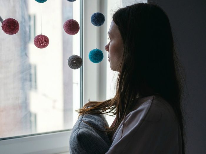A woman hugging a cushion looks out of the window
