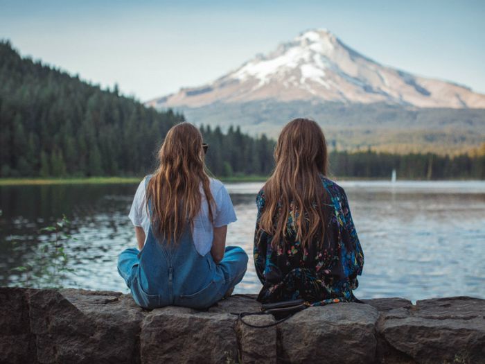 Sisters sitting by a lake in front of a mountain