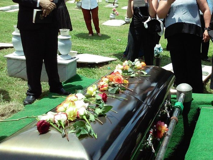 People standing around a coffin with flowers on top before it is lowered into a grave